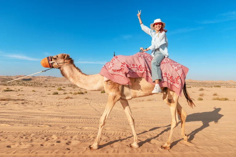smiling-female-tourist-riding-dromedary-camel-desert-sunny-day